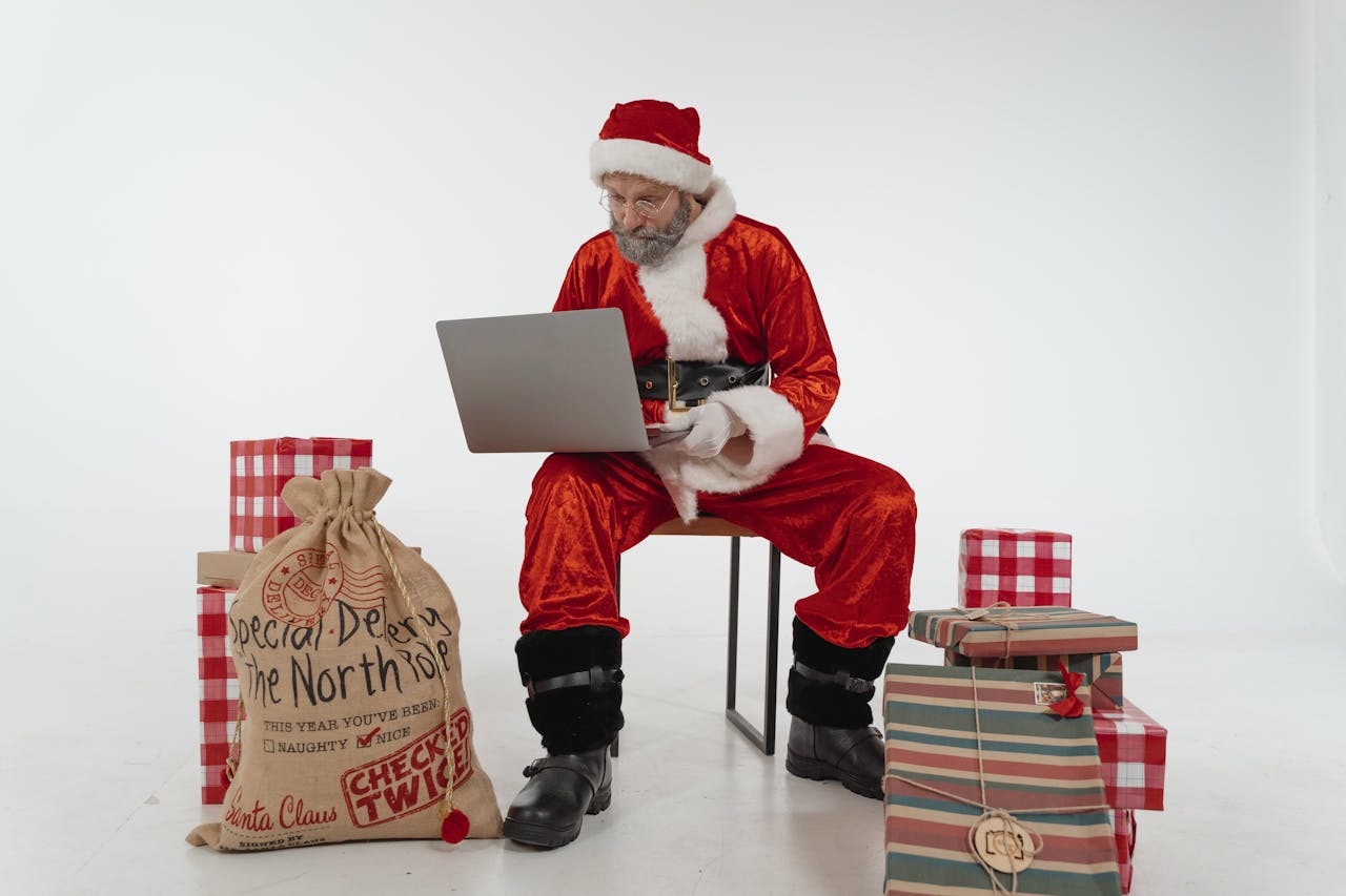 π Top 10 Trending Christmas Gifts in India 2025 Elderly Santa using a laptop surrounded by Christmas gifts in a studio.