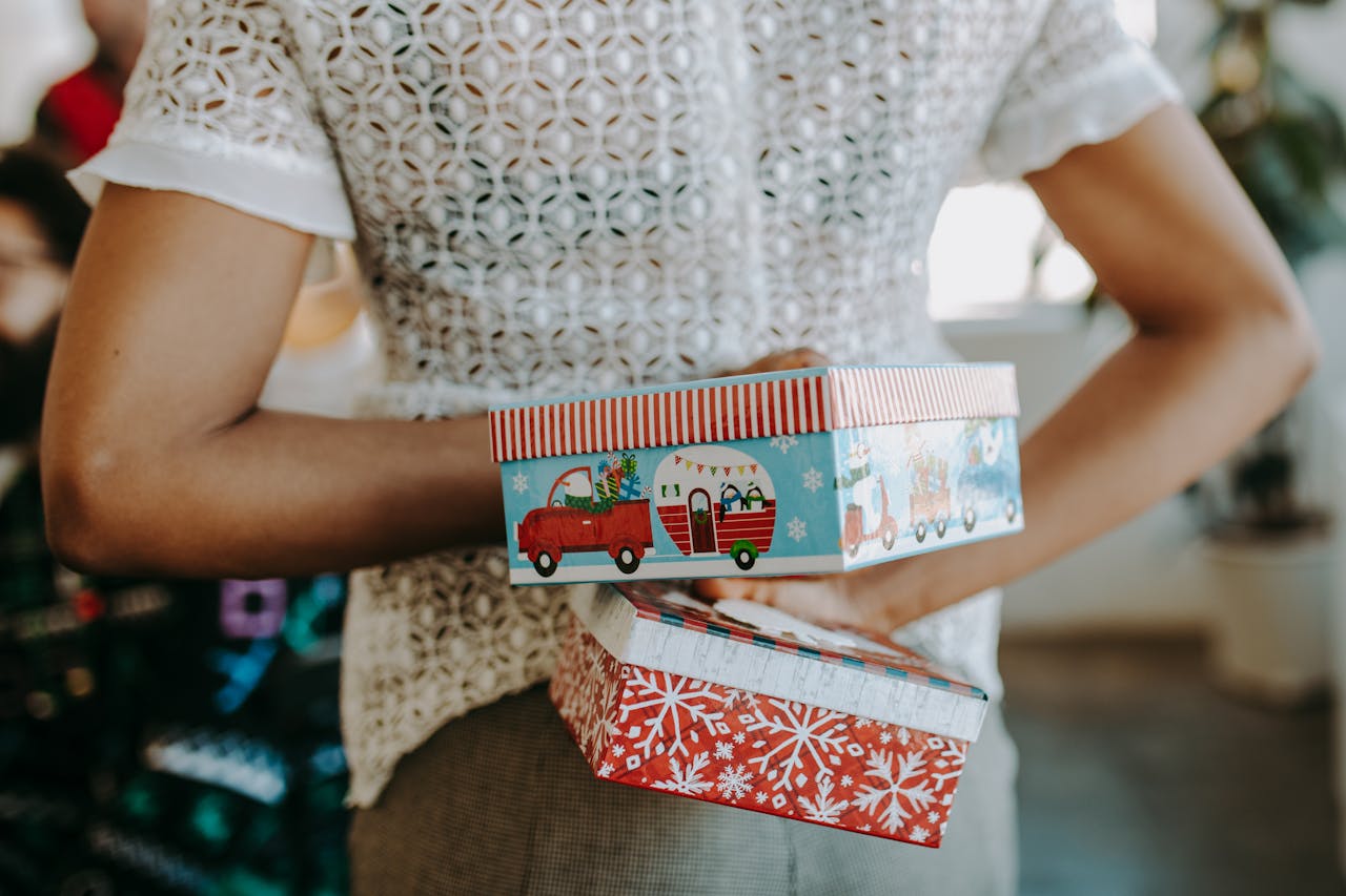 Person hiding colorful Christmas gift boxes behind their back, creating a playful festive surprise.